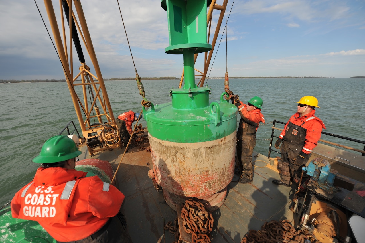 Coast Guardsmen lower a green buoy onto the deck of their boat.