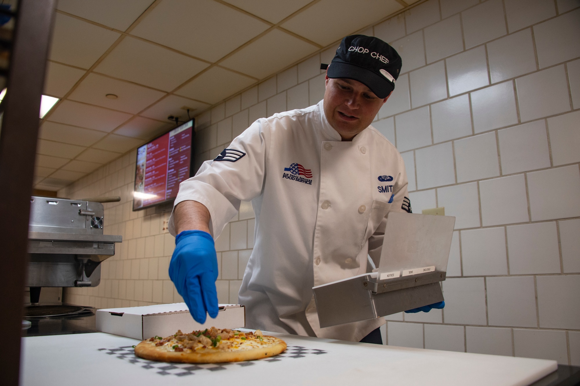 U.S. Air Force Senior Airman Dylan Smith, a food services journeyman assigned to the 97th Force Support Squadron, puts toppings on a pizza, March 26, 2019, at Altus Air Force Base, Okla. Hangar 97 has a pizza oven that can make pizzas fresh and to custom order. (U.S. Air Force photo by Senior Airman Cody Dowell)
