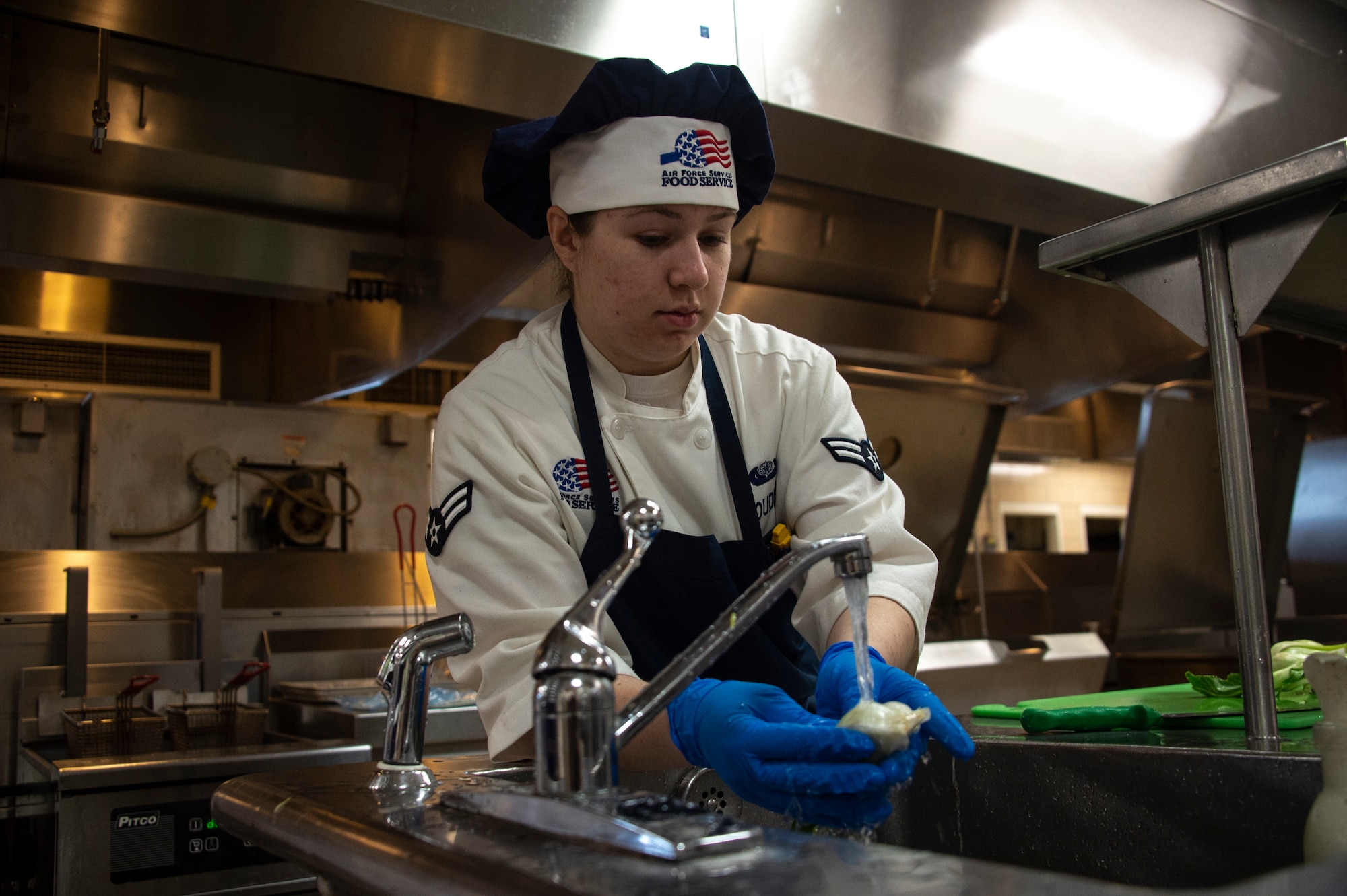 U.S. Air Force Airman 1st Class Bethany Doudna, a food services apprentice assigned to the 97th Force Support Squadron, washes bok choy in a sink, March 26, 2019, at Altus Air Force Base, Okla. One of the stations at Hangar 97 changes quarterly with different food options. (U.S. Air Force photo by Senior Airman Cody Dowell)
