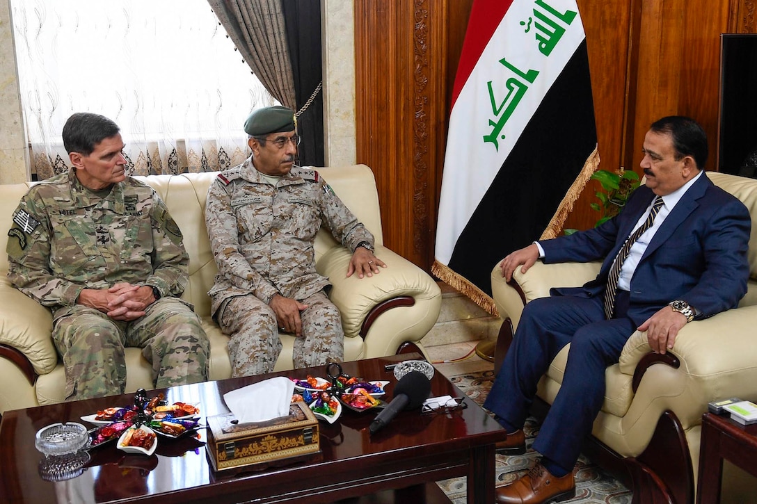 Two generals in uniform sit on a couch facing a man in a civilian suit.