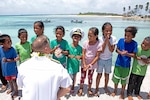 Rear Adm. Joey Tynch, Commander, Task Force 73, talks with Marshallese children on the Enniburr pier after arriving for a ground-breaking ceremony during Pacific Partnership 2019. Pacific Partnership, now in its 14th iteration, is the largest annual multinational humanitarian assistance and disaster relief preparedness mission conducted in the Indo-Pacific. Each year, the mission team works collectively with host and partner nations to enhance regional interoperability and disaster response capabilities, increase stability and security in the region, and foster new and enduring friendships in the Indo-Pacific.