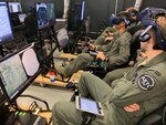 Royal Air Force Flight Officer Syd Janota (foreground), Pilot Training Next 2.0 student, observes a fellow student flying a virtual-reality training sortie at the PTN facility at the Armed Forces Reserve Center in Austin, Texas, March 18, 2019. The RAF have both a student-pilot and an instructor pilot participating in the class as they look to introduce PTN lessons learned into their flying training pipeline.
