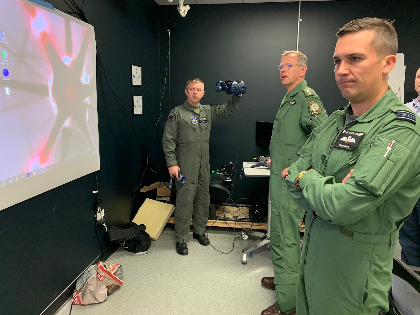 Royal Air Force Flight Lt. Darren French, Pilot Training Next 2.0 instructor pilot and the RAF's senior national representative, highlights virtual-reality headset capabilities to British Army Col. Paddy Logan (center), assistant director for flying training for RAF Headquarters 22 Group, and RAF Squadron Leader Steve Smith (left) at the PTN facility at the Armed Forces Reserve Center in Austin, Texas, March 18. The RAF have both a student-pilot and an instructor pilot participating in the class as they look to introduce PTN lessons learned into their flying training pipeline.