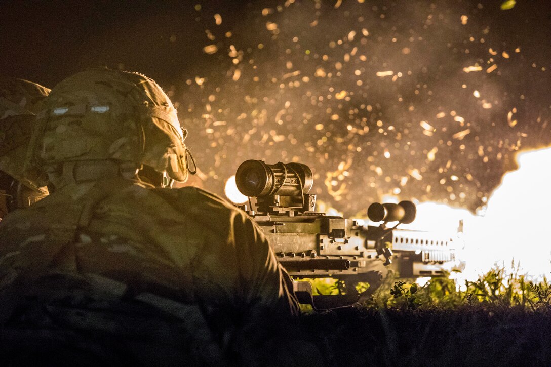 A solider fires a weapon at night.