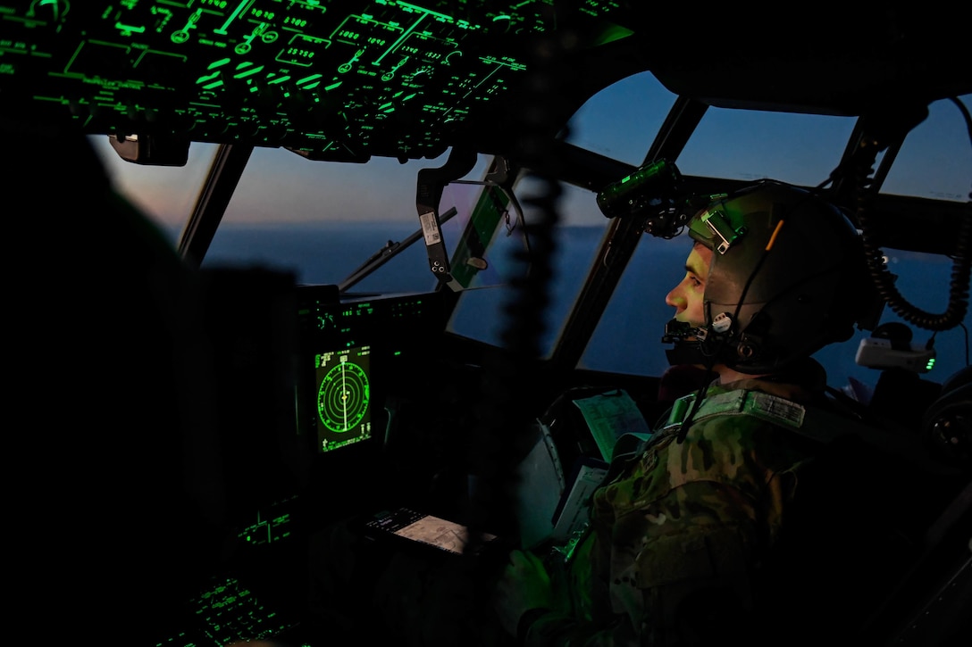 Airmen pilot an aircraft in a darkened cockpit illuminated by green instrument panels.