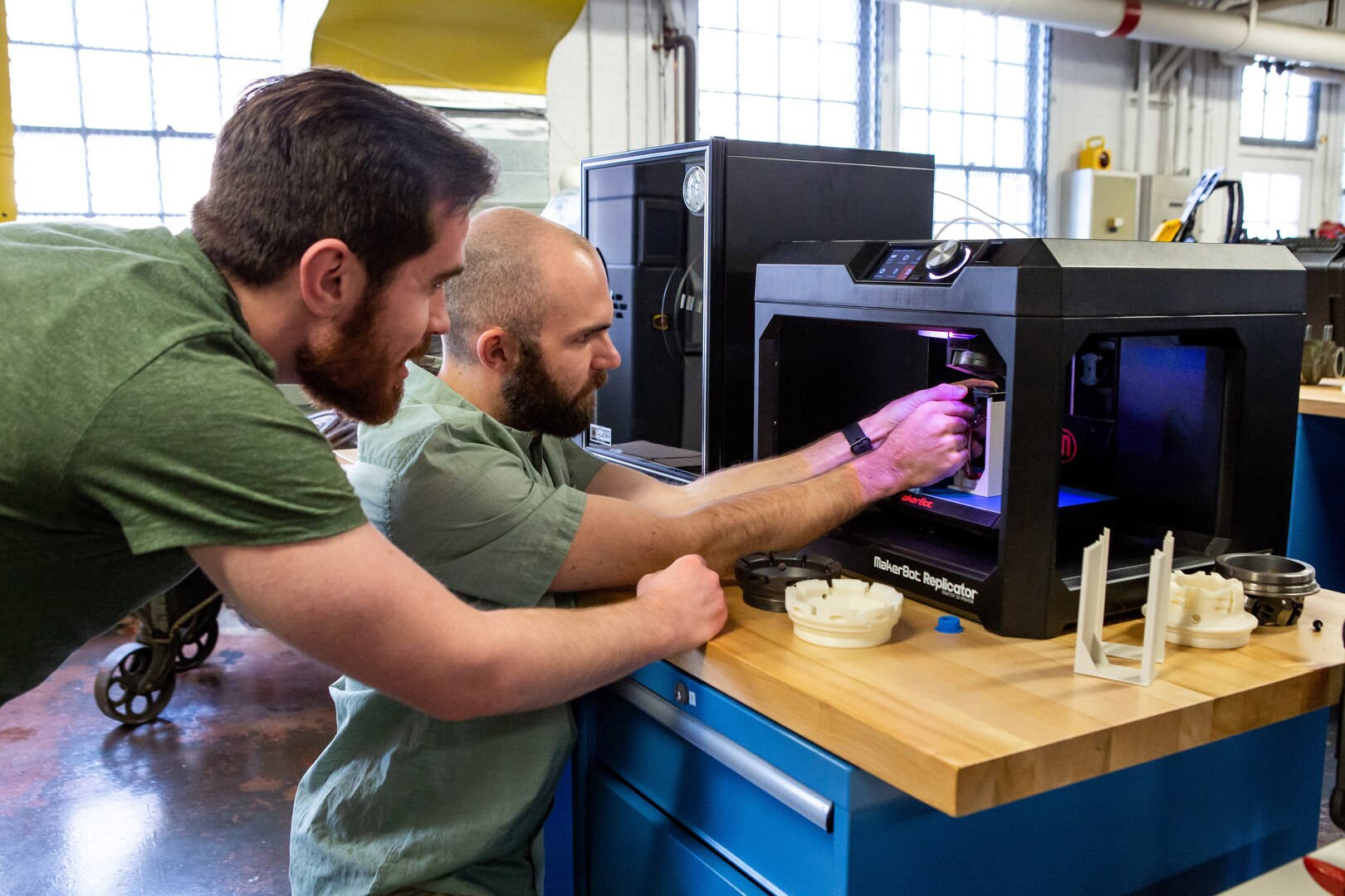 Brendon Wilkins and Matthew Perkinson from Norfolk Naval Shipyard's Technology and Innovation (T&I) Lab, work on a 3-D printer.