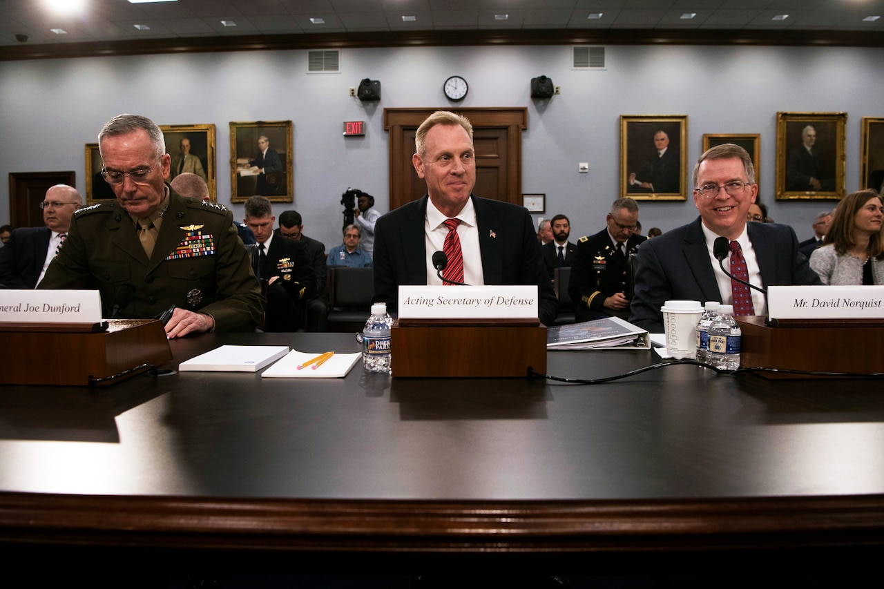 Three defense leaders sit behind a long desk.