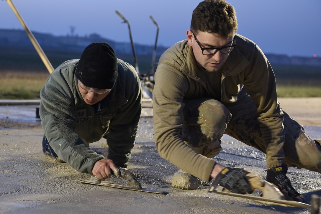 (Left) U.S. Air Force Tech Sgt. Jonathan Shinsato and Staff Sgt. Jeffrey Deptula, 8th Civil Engineer Squadron pavement and construction equipment journeymen, smooth wet concrete on the flight line at Kunsan Air Base, Republic of Korea, May 2, 2019. The 8th CES conducted a rapid response to a rupture that opened on the runway, and repaired the flight line within 24 hours. (U.S. Air Force photo by Staff Sgt. Joshua Edwards)
