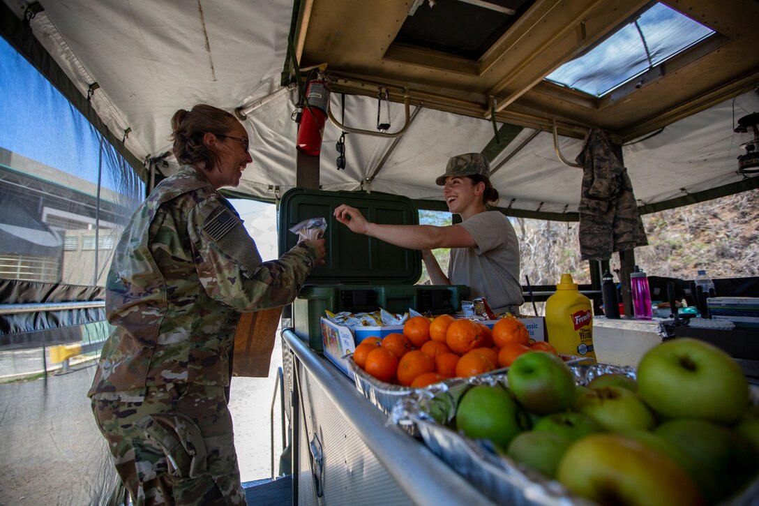 U.S. Air Force Tech. Sgt. Micah M. Gill, a services journeyman with 185th Air Refueling Wing (right), passes a sandwich to another Airman at Yauco, Puerto Rico, April 30, 2019, during Innovative Readiness Training Puerto Rico. The purpose of the IRT Puerto Rico is to provide dental, optometry and medical care to the community while performing joint military humanitarian operations. Marine Forces Reserve is participating in IRT Puerto Rico 2019 in order to maintain military readiness while strengthening alliances with partners. (U.S. Marine Corps photo by Sgt. Andy O. Martinez)