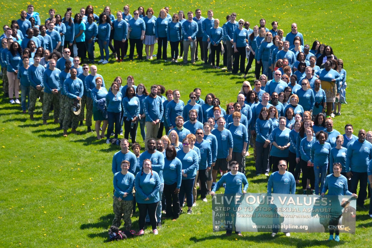 A large group of people stand in formation wearing teal shirts.