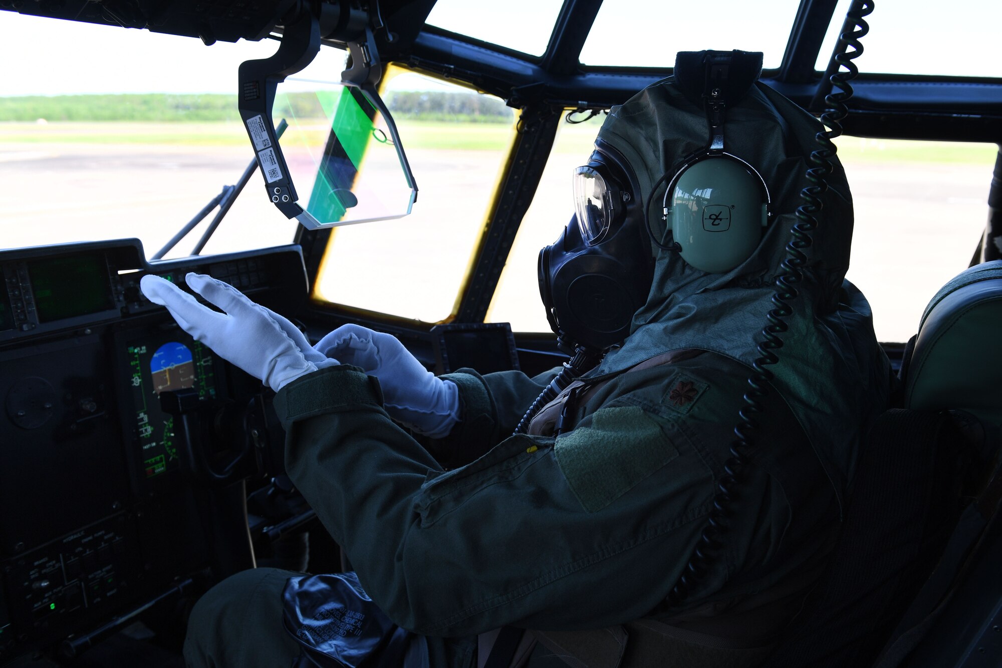 A pilot puts on gloves in the cock pit of a C-130J