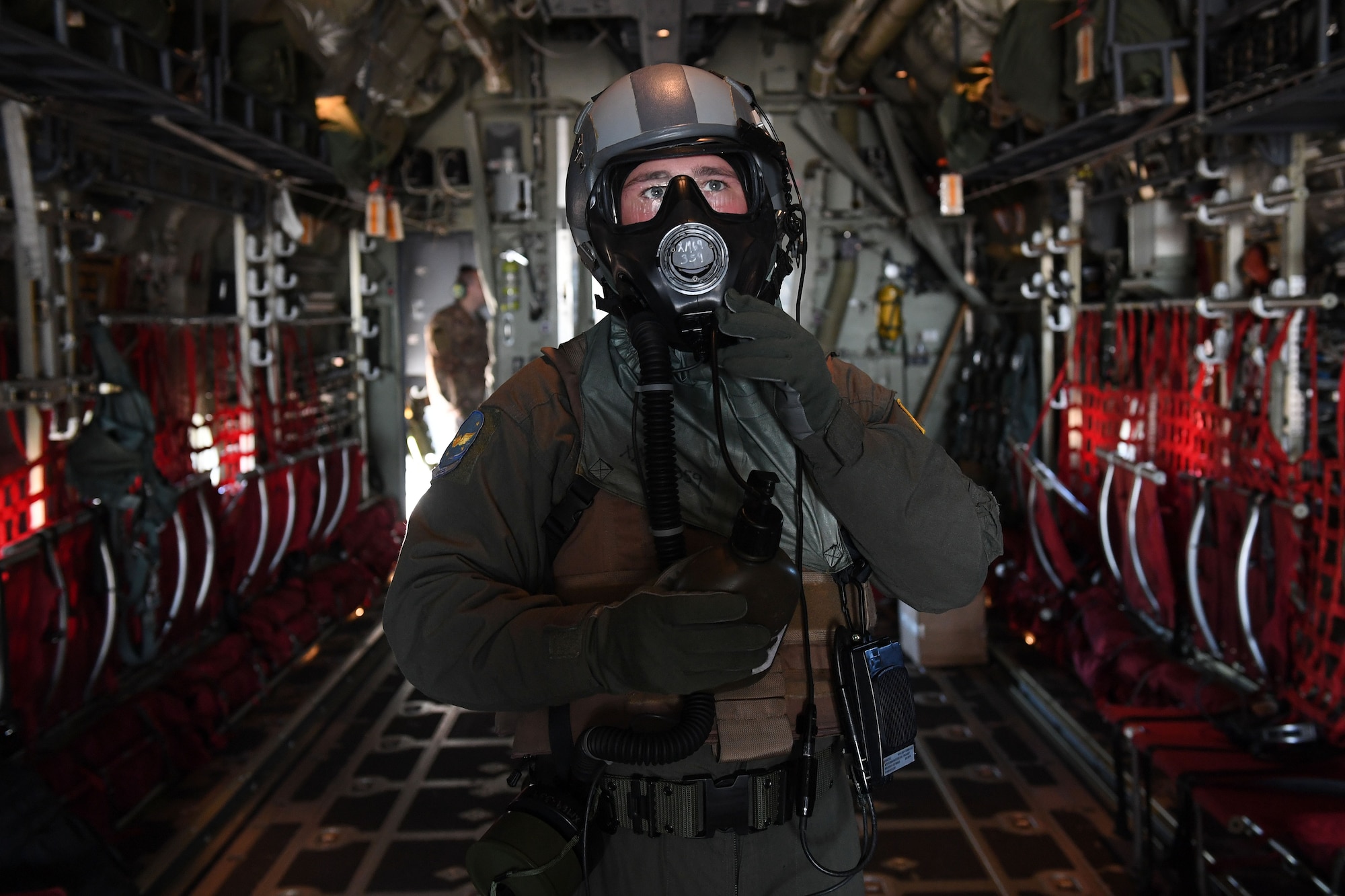 A loadmaster wears a gas mask in the back of a C-130J