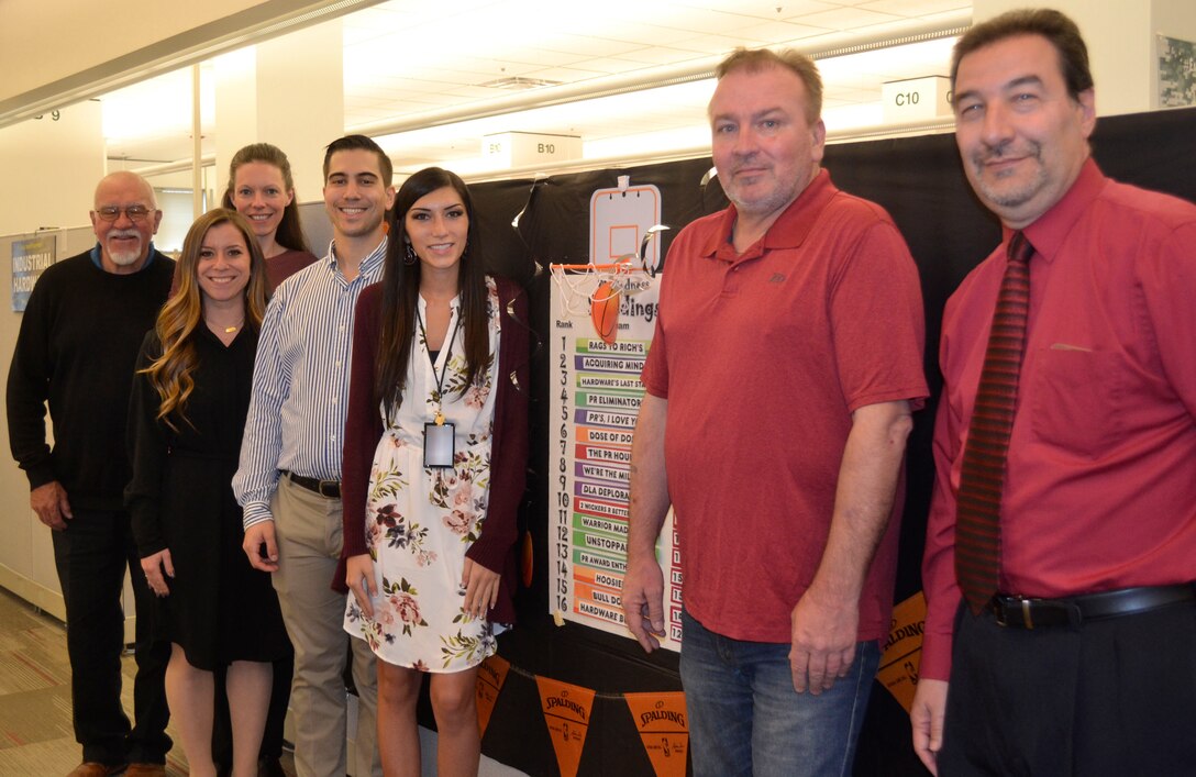 Teammates from DLA Troop Support Industrial Hardware and members of PR Madness’ first place finishers, “Rags to Rich’s,” pose in front of this year’s PR Madness leaderboard May 1, 2019 in Philadelphia.