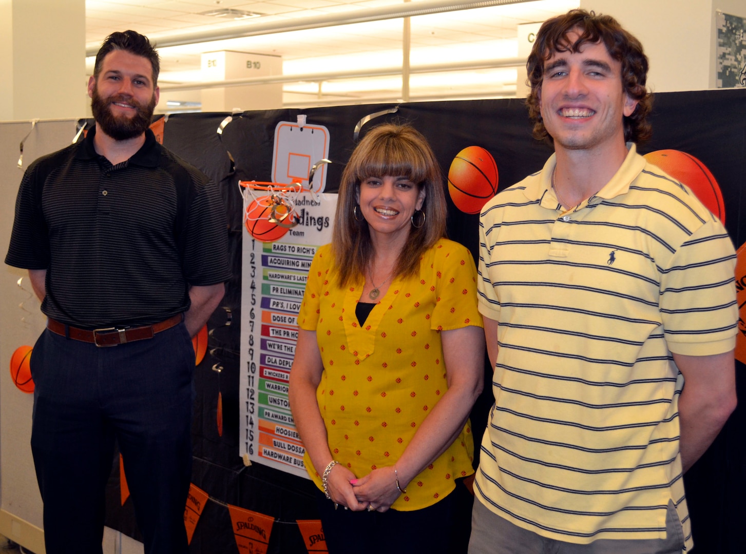 Teammates Matt Eckenrode, Cynthia Linsalata and Jonathan Ferrante, employees from DLA Troop Support Industrial Hardware and members of PR Madness’ second place finishers, “Acquiring Minds,” pose in front of this year’s PR Madness leaderboard April 30, 2019 in Philadelphia.