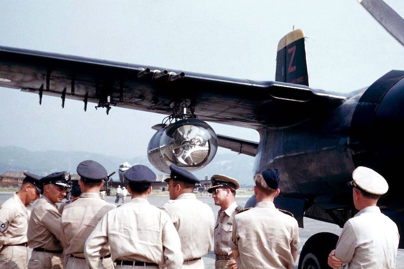 Eight uniformed service members stand beside the searchlight attached to a B-26 Invader.