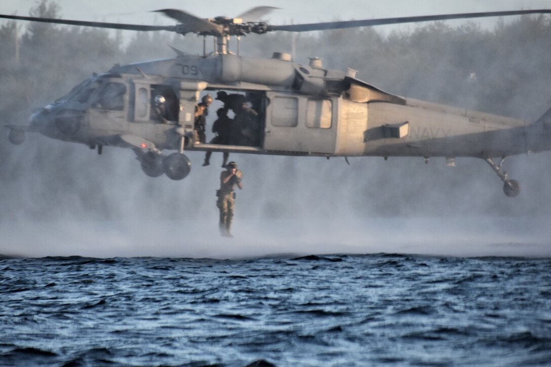 Sailors jump out of an aircraft into a body of water.