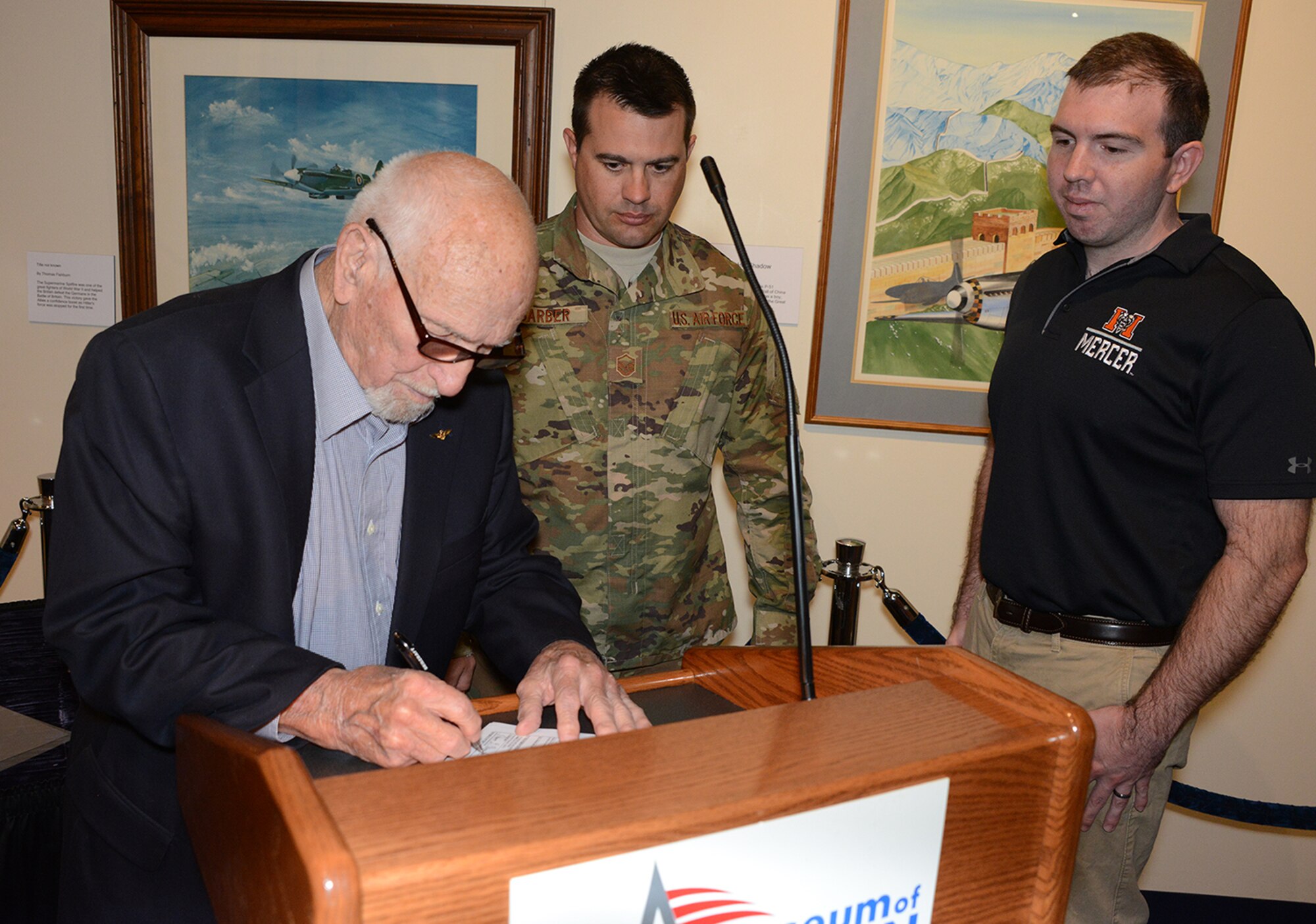 Ramon Carpenter, a retired United States Naval aviator, signs the required paperwork after performing his grandson's commissioning oath. Master Sgt. David Barber, an officer accessions recruiter assigned to Dobbins Air Reserve Base, Georgia, served as  Garren "Ridge" Belflower's recruiter. The oath took place at the Museum of Aviation at Robins Air Force Base, Georgia. Belflower joins a long list of family members who have served in the United States military. (Air Force photo/Master Sgt. Chance Babin)