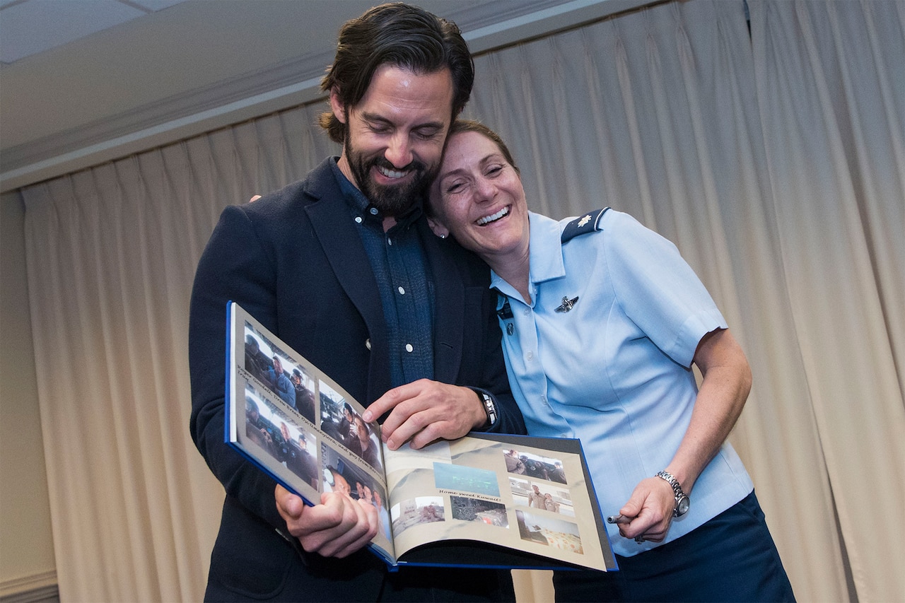 A man holding a scrapbook laughs with a female airman, who is hugging the man from the side.