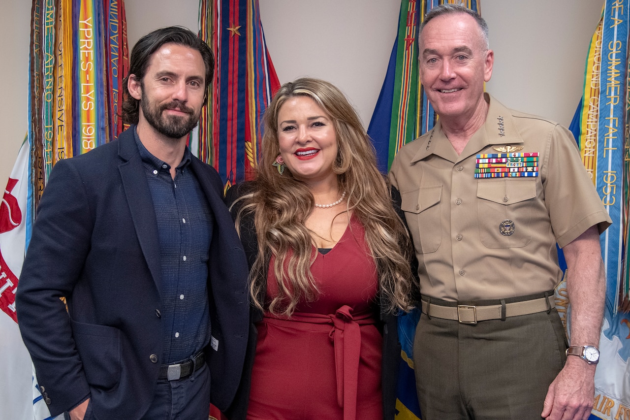 A man and a woman poses with a Marine Corps general in front of several flags.