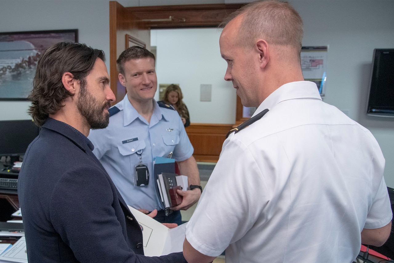 A man holding a book chats with two military service members inside an office.