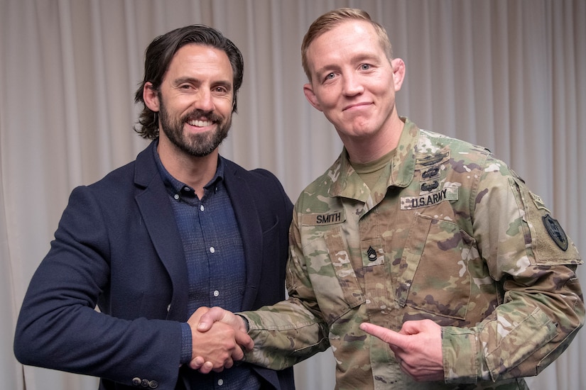 A man shakes the hand of a service member who is looking at the camera and pointing back at the man.