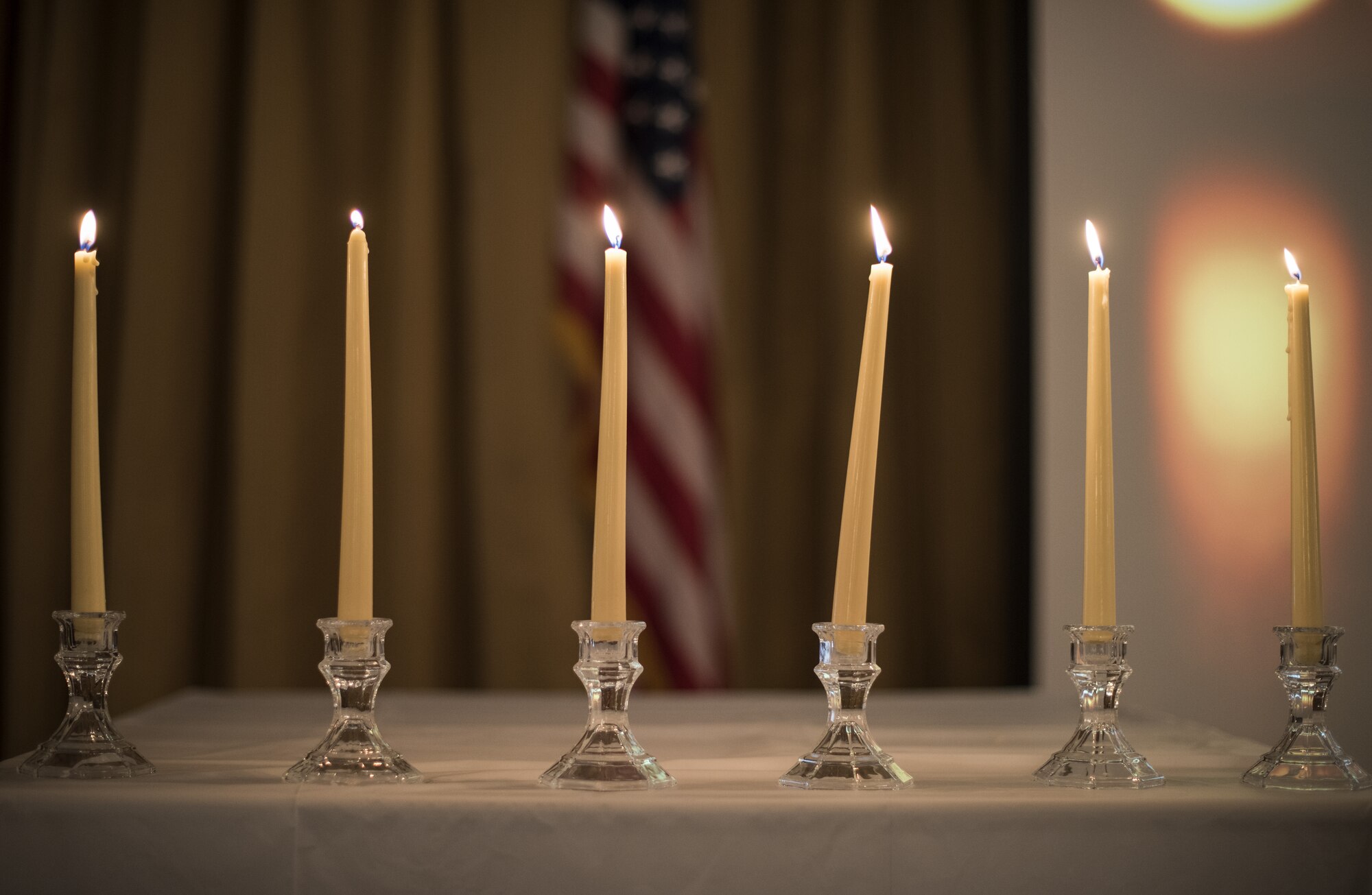 Six lit candles line the edge of a table during the 2019 A Day of Remembrance ceremony on Joint Base McGuire-Dix-Lakehurst, New Jersey, April 30, 2019. Each candle represents one million people and six candles are lit for the six million people that were killed during the Holocaust. In some communities, seven candles are lit, thereby linking up to the menorah symbolism. (U.S. Air Force photo by Airman 1st Class Ariel Owings)