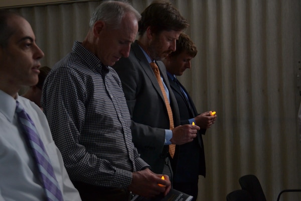 Four men bow their heads and hold candles during a moment of silence