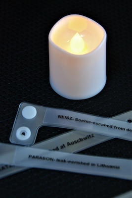 A tea light candle glows around wrist bands bearing names of Holocaust victims