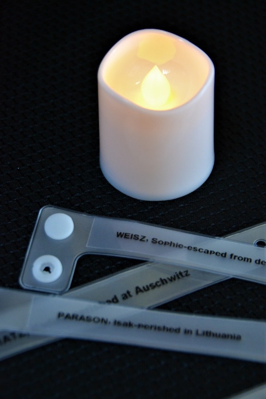 A tea light candle glows around wrist bands bearing names of Holocaust victims