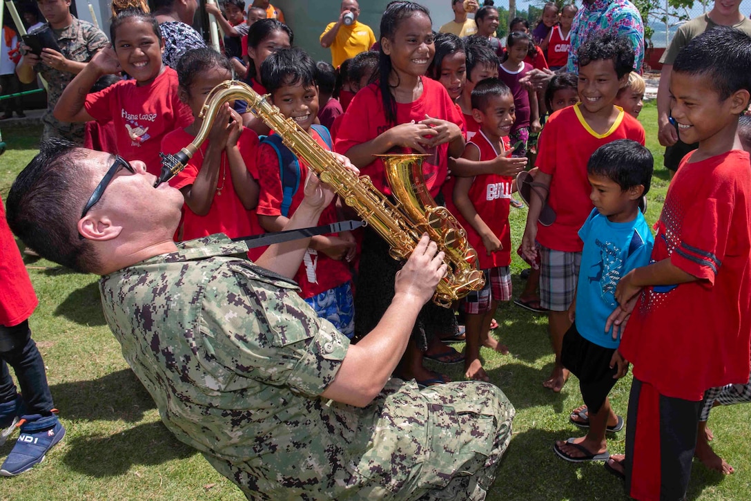 A sailor plays the saxophone for a group of children.