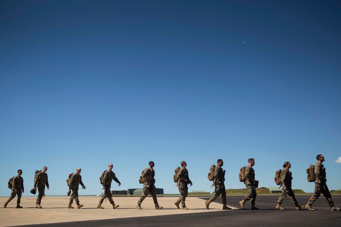 A line of Marines walk behind each other along a tarmac at an Air Force base.