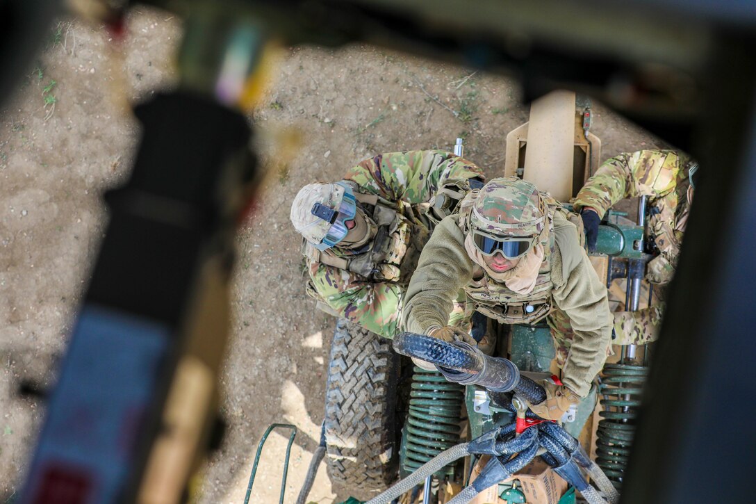 A look down at a soldier holding a hook while two soldiers stand on either side.