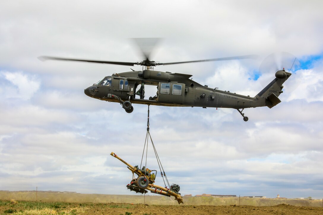 A military helicopter flying with with a large weapon attached to the bottom.