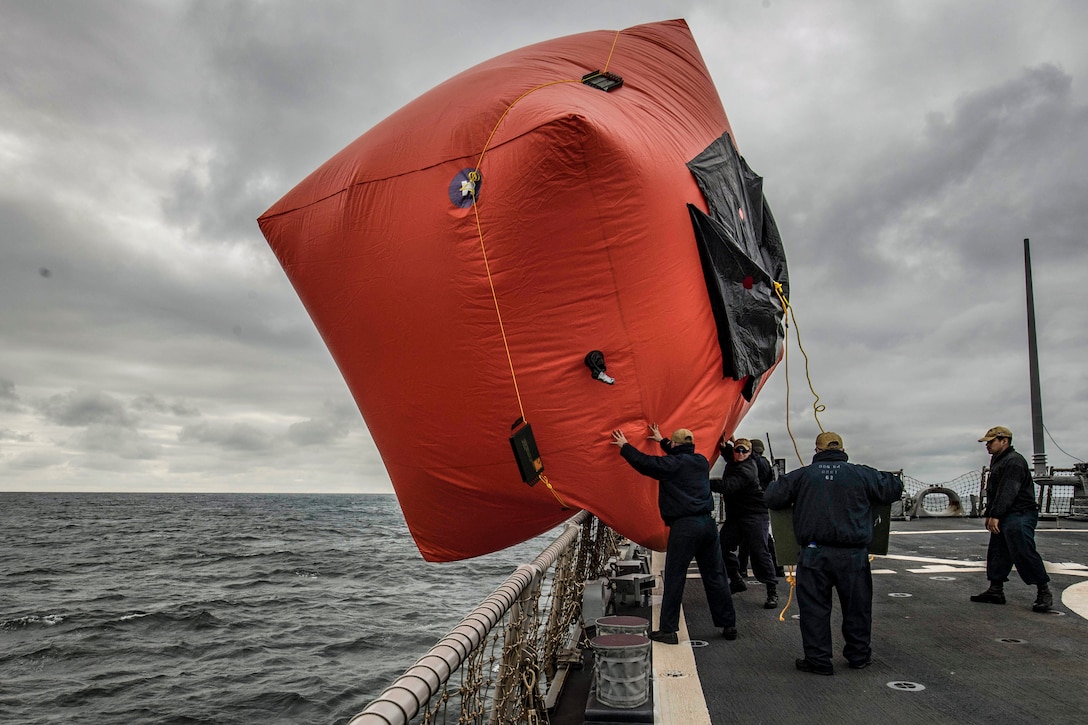 Sailors push a big red inflatable target off the side of a ship into the water.