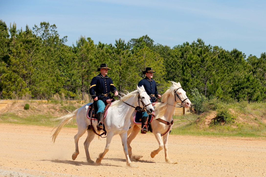 Two soldiers ride horses along a dirt road.