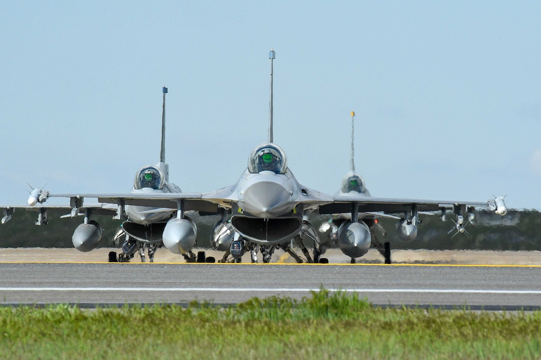 Three military jets sit in a triangular formation on the tarmac.