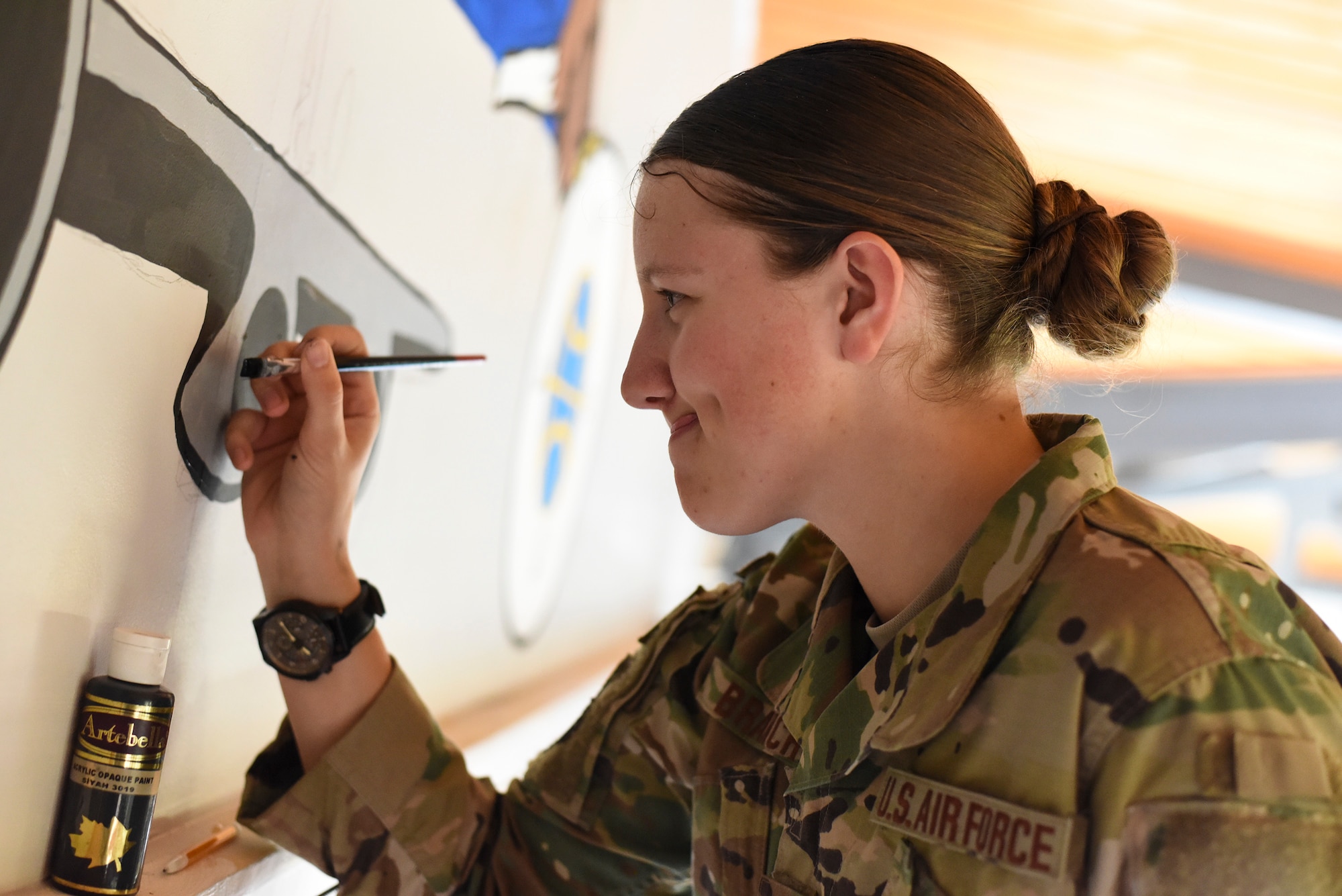 Airman First Class Amber Branch, 728th Air Mobility Squadron passenger services agent, paints a C-5 Galaxy on a mural in the squadron’s heritage room Feb. 1, 2019, at Incirlik Air Base, Turkey. The mural consisted of a yellow background, a blue folded flag, an eagle, a soldier’s cross silhouette, a compass, a K-loader and a C-5 Galaxy. (U.S. Air Force photo by Staff Sgt. Ceaira Tinsley)