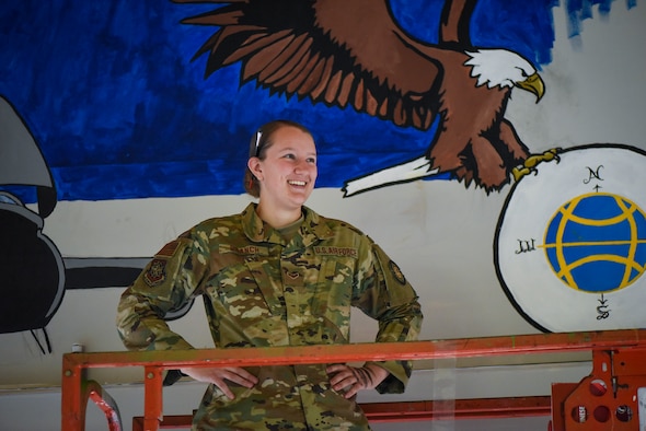 Airman First Class Amber Branch, 728th Air Mobility Squadron passenger services agent, poses for a photo in front of a mural in the squadron’s heritage room Feb. 1, 2019, at Incirlik Air Base, Turkey. Branch used the mural as an opportunity to combine her love for her job with her love for drawing. (U.S. Air Force photo by Staff Sgt. Ceaira Tinsley)