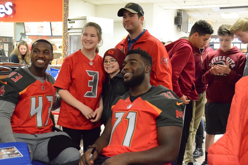 A man and two children pose for a photo with two professional football players.