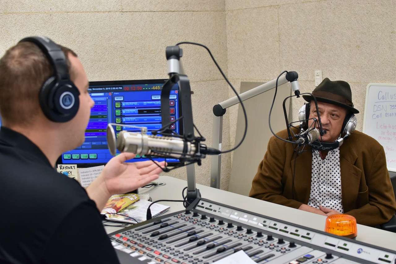 Two men speak into microphones in a radio studio.