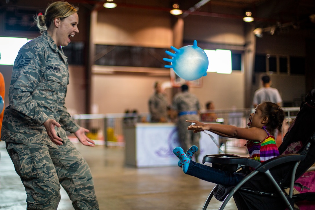 An airman stands smiling as a child throws a balloon towards her.