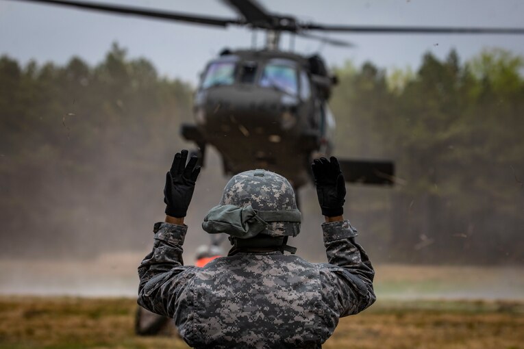 A soldier holds both hands up toward a helicopter in the distance.