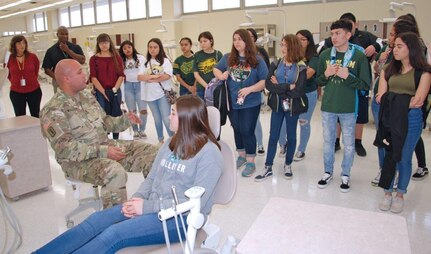 Staff Sgt. James Mcalister, NCOIC Dental Department, Preventative Medicine, briefs students on the training and equipment used in the dental program while Taetum, a freshman in McCollum High School's health science class sits in the hot seat. Taetum plans to be a cardiac thorasic surgeon after college.