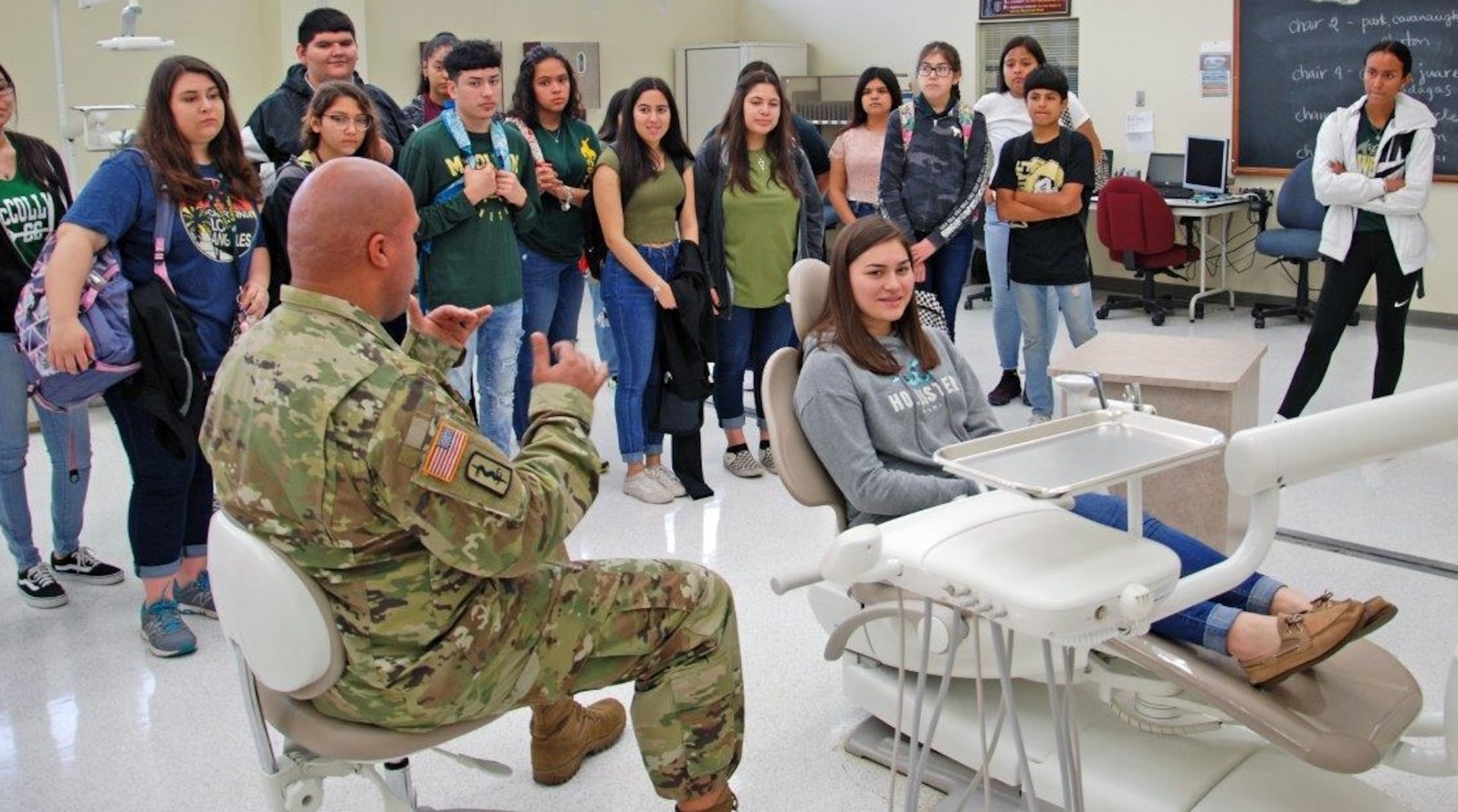 Staff Sgt. James Mcalister, NCOIC Dental Department, Preventative Medicine, briefs students on the training and equipment used in the dental program while Taetum, a freshman in McCollum High School's health science class sits in the hot seat. Taetum plans to be a cardiac thorasic surgeon after college.