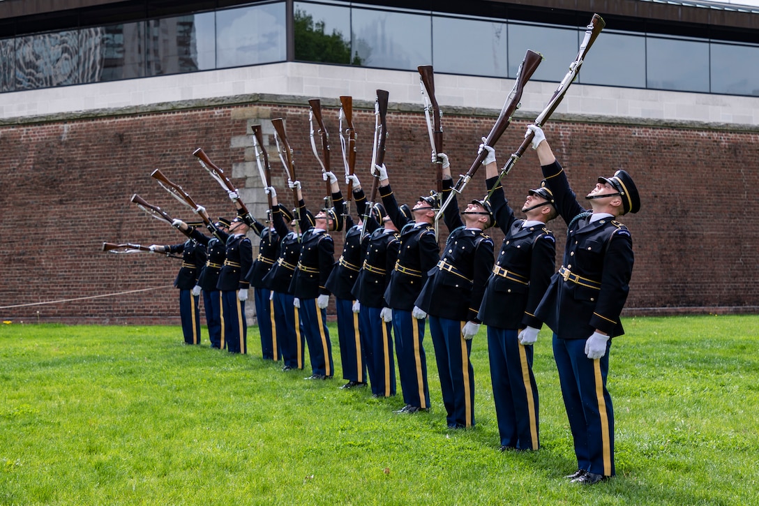 Soldiers stand in a line twirling their weapons during a performance.