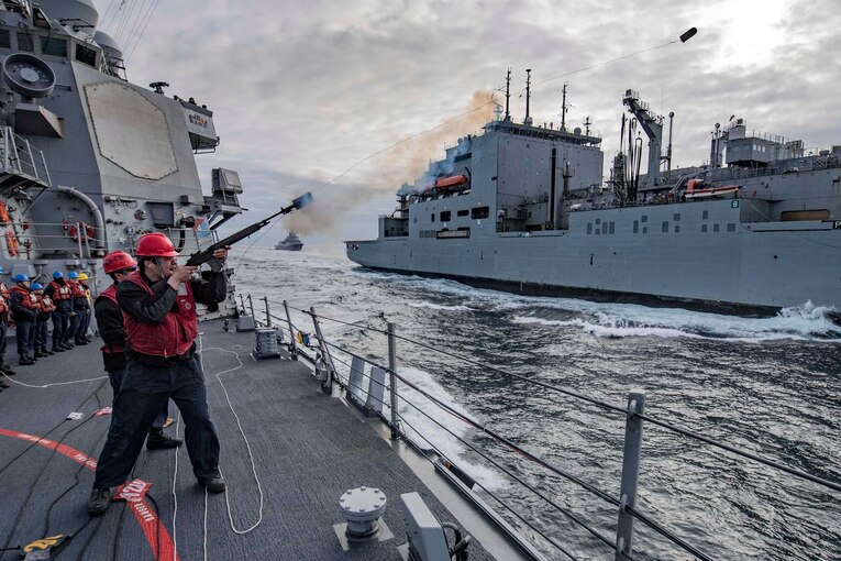 A sailor fires a shot line from one ship to another.