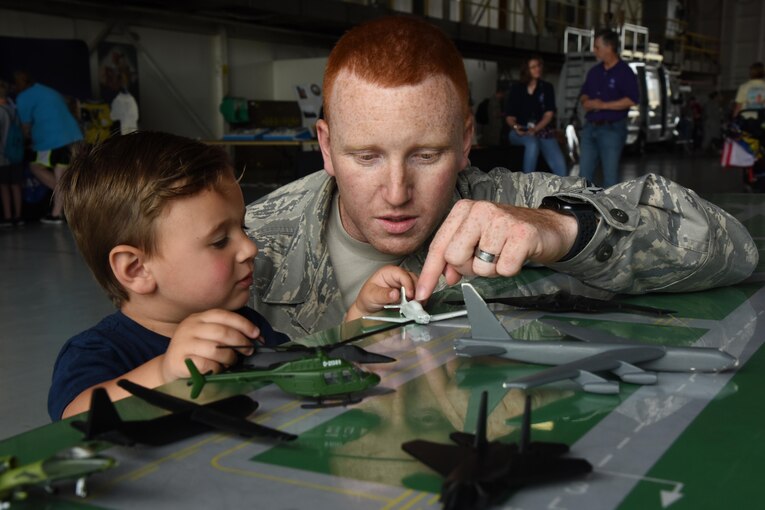 An airman uses a toy airplane to teach a young child about air traffic control.