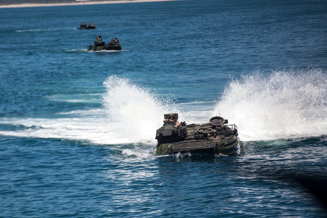 Three amphibious assault vehicles move through water in a formation.