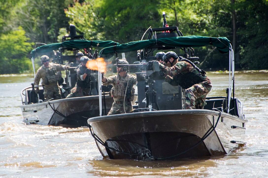 A man fires a weapon from the deck of a patrol boat as another man guides him and a second boat follows.