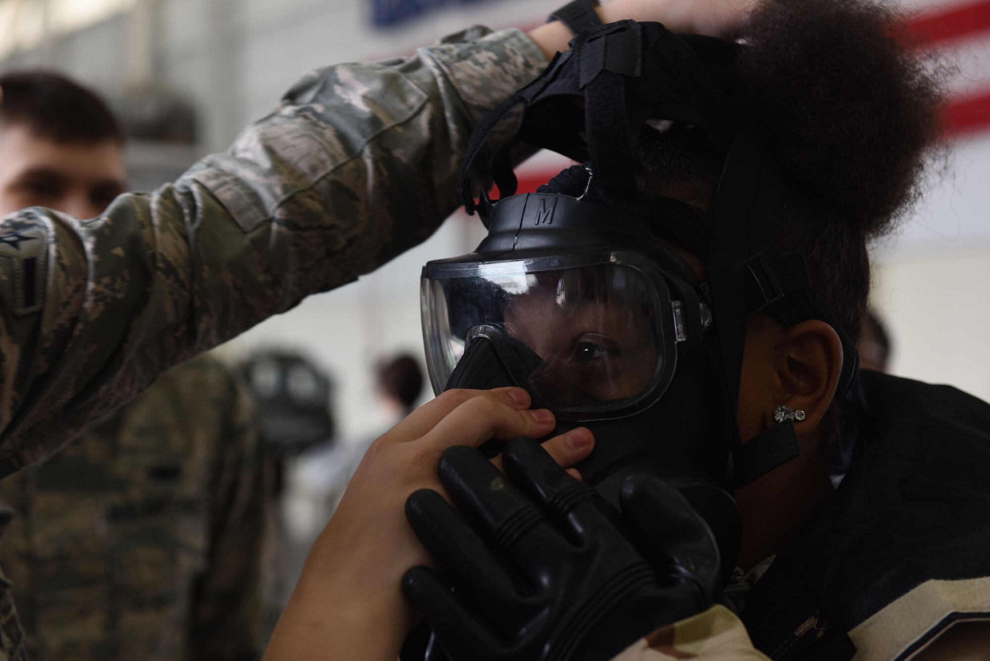 A girl wearing protective military gear puts on a gas mask